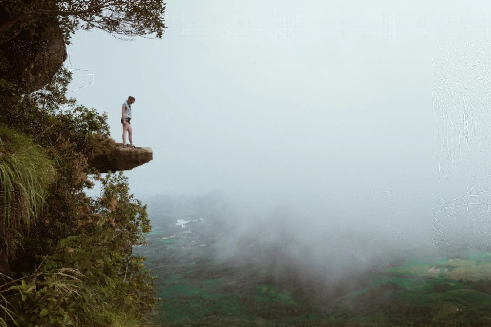 Person standing on a misty cliff edge overlooking a foggy valley
