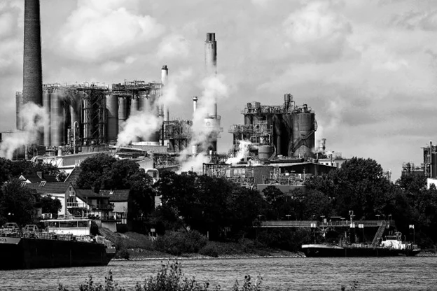 Black-and-white photo of an industrial complex with smokestacks beside a river