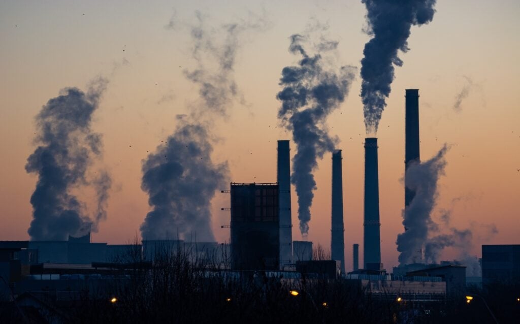Industrial smokestacks emitting smoke against a sunset sky