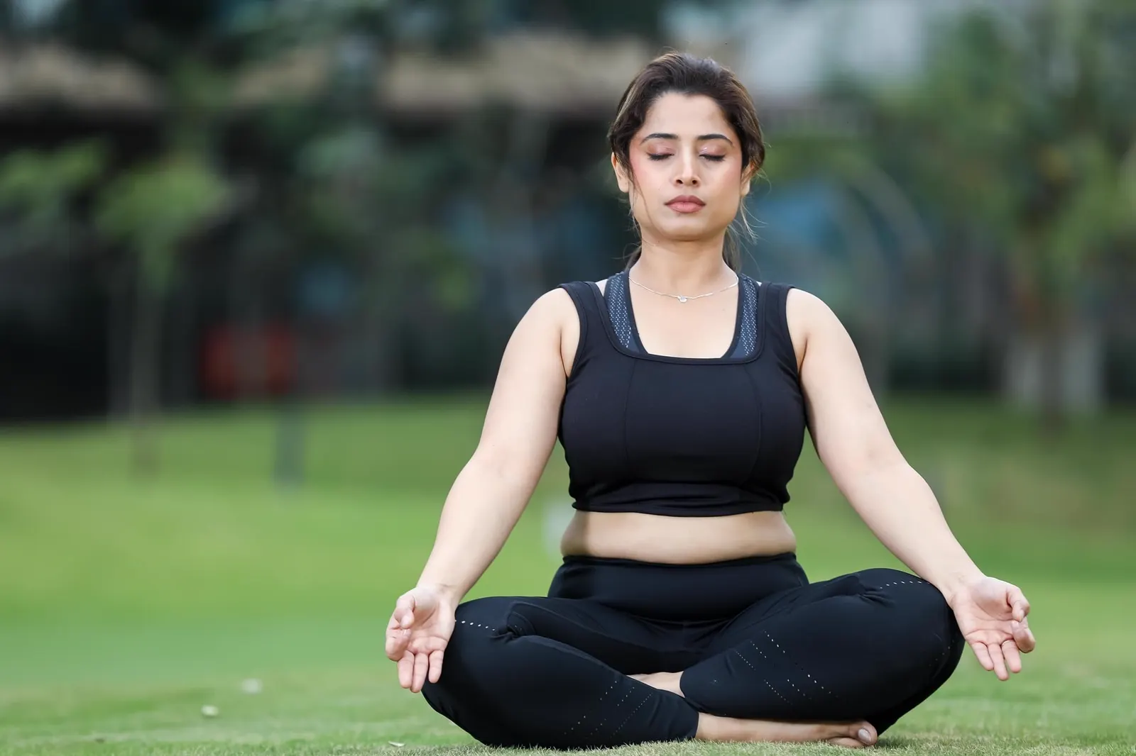 Woman sitting cross-legged on green grass with eyes closed, breathing deeply