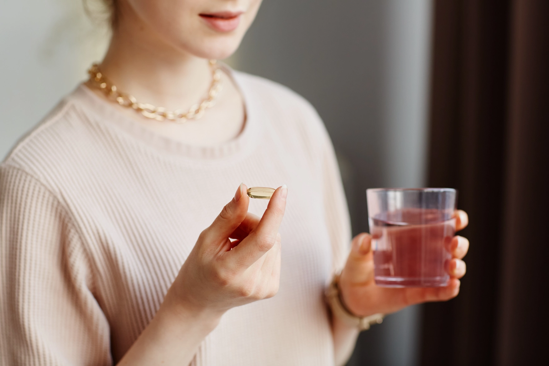 Woman holding a supplement capsule and a glass of water