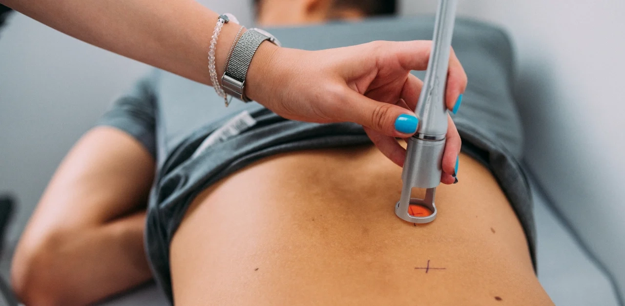 Clinician applying a handheld K-Laser device to a patient’s lower back during therapy