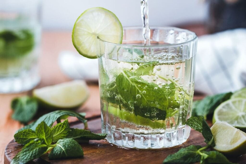 A glass of water being poured, garnished with lime slices and fresh mint leaves