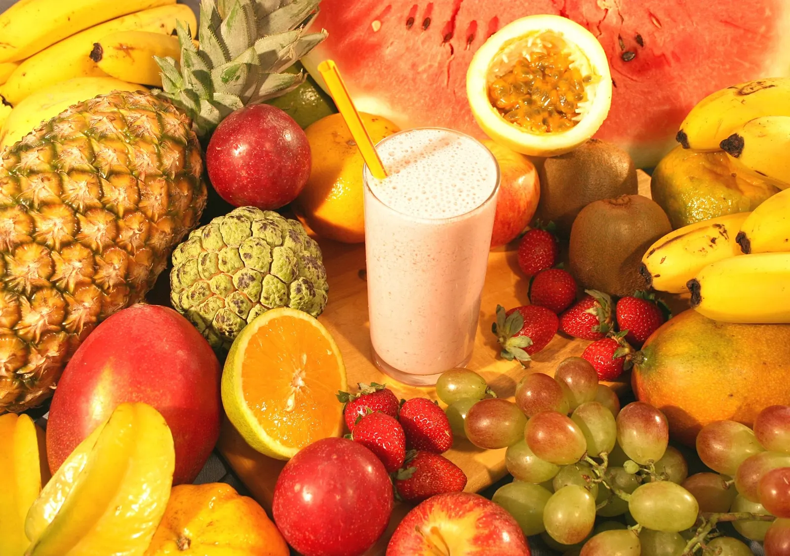 Table full of fresh vitamin C rich fruit including oranges, strawberries, kiwi and pineapple beside a smoothie