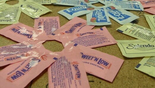 Various artificial sweetener packets including pink Sweet'N Low, blue Equal, and yellow Splenda
