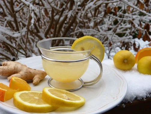 Warm honey-lemon ginger tea on a snowy outdoor table, surrounded by lemons and ginger