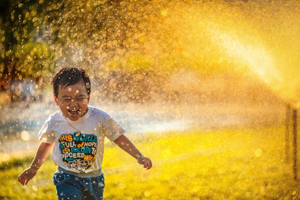 Image of a little boy running through a sprinkler to illustrate the joy of not having adhd symptoms in kids.